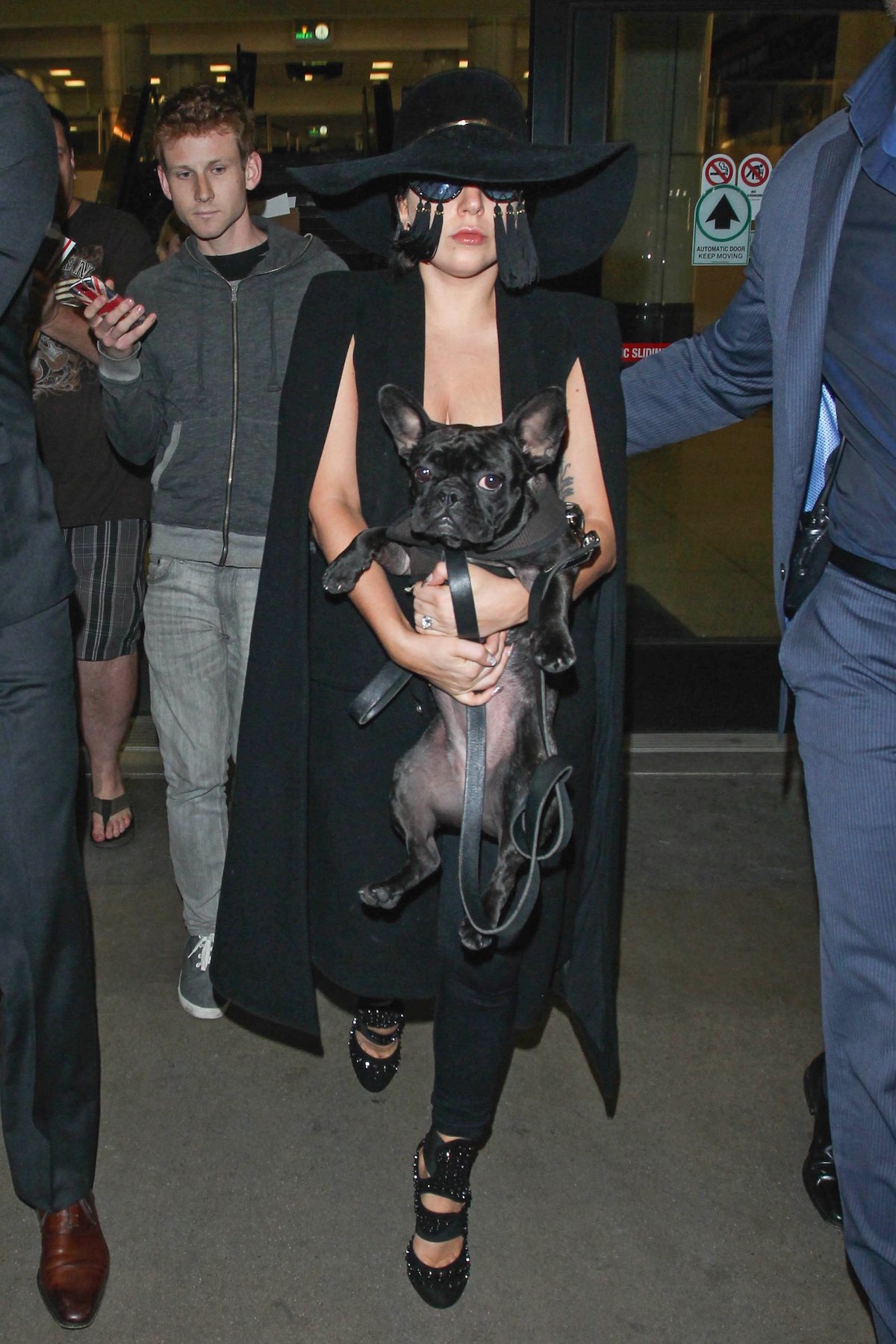 Lady Gaga in a black outfit and hat, holding a black dog.