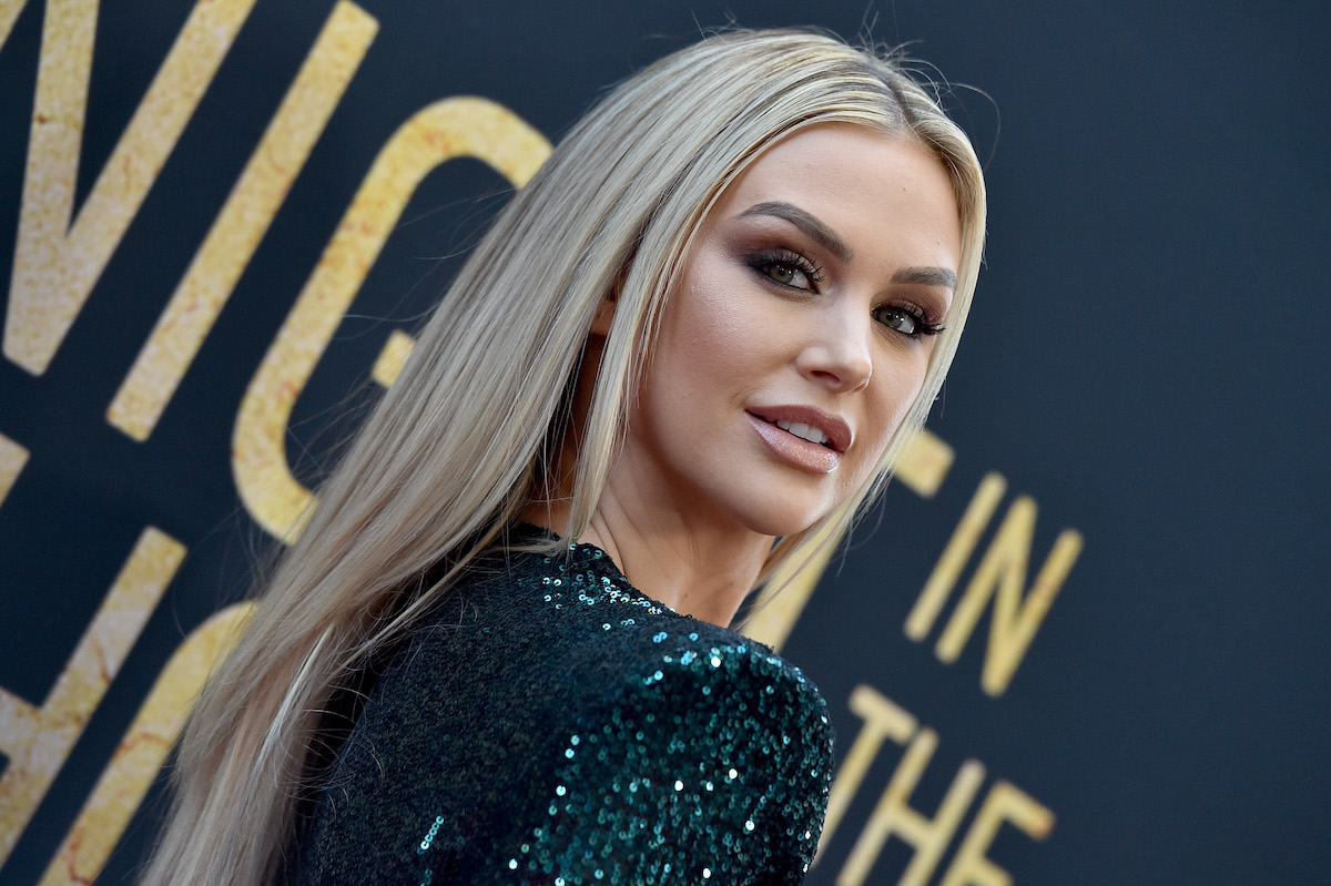 Lala Kent wears a sparkly green dress and looks over her shoulder at the camera, smiling.
