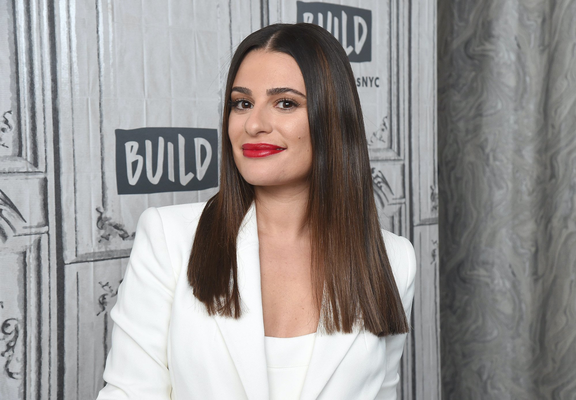 Lea Michele smiling in front of a gray background