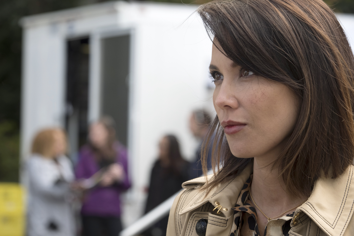Lexa Doig in a trench coat looking off to the distance.