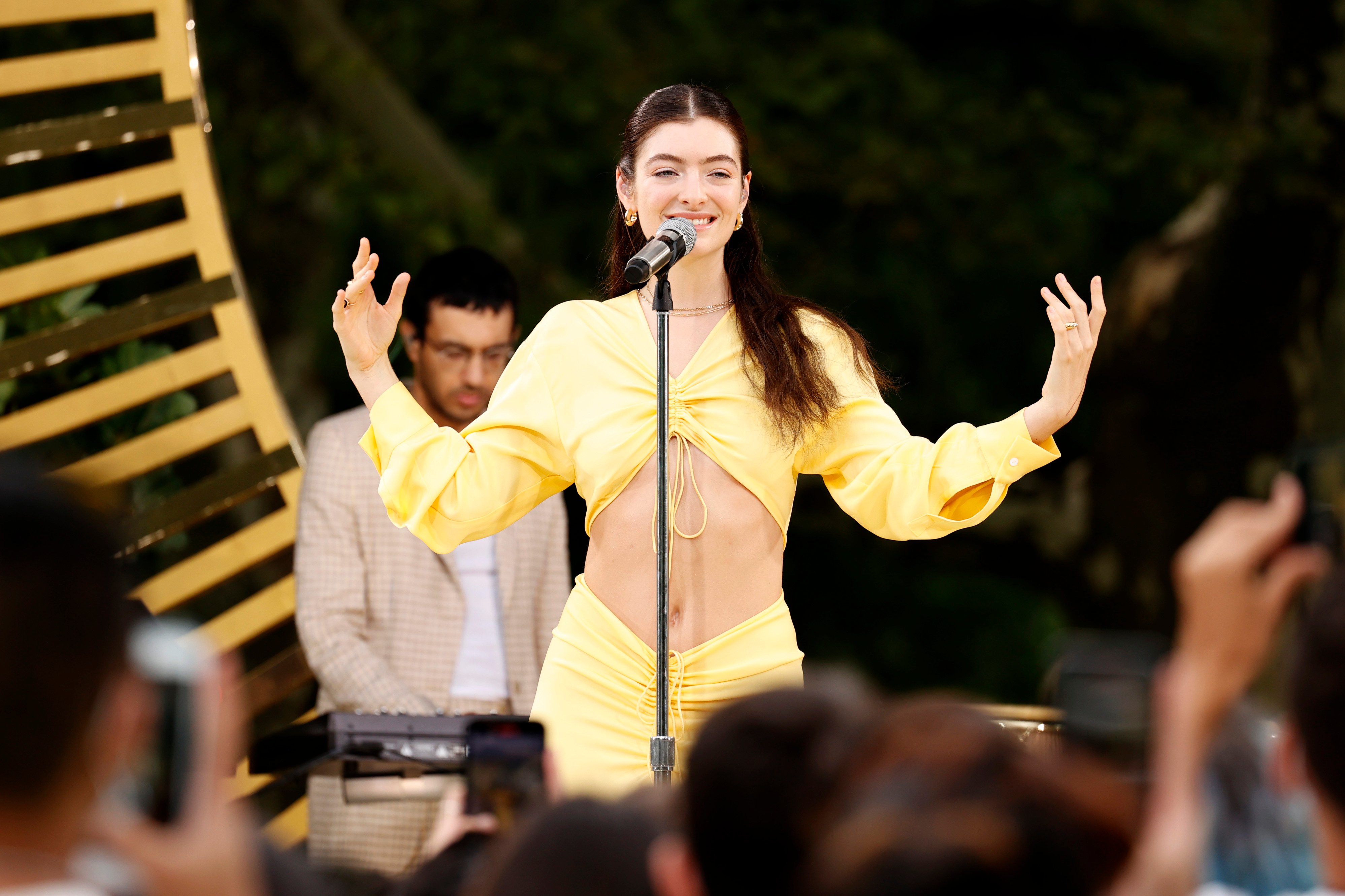 Lorde performing on stage in a yellow shirt and skirt.
