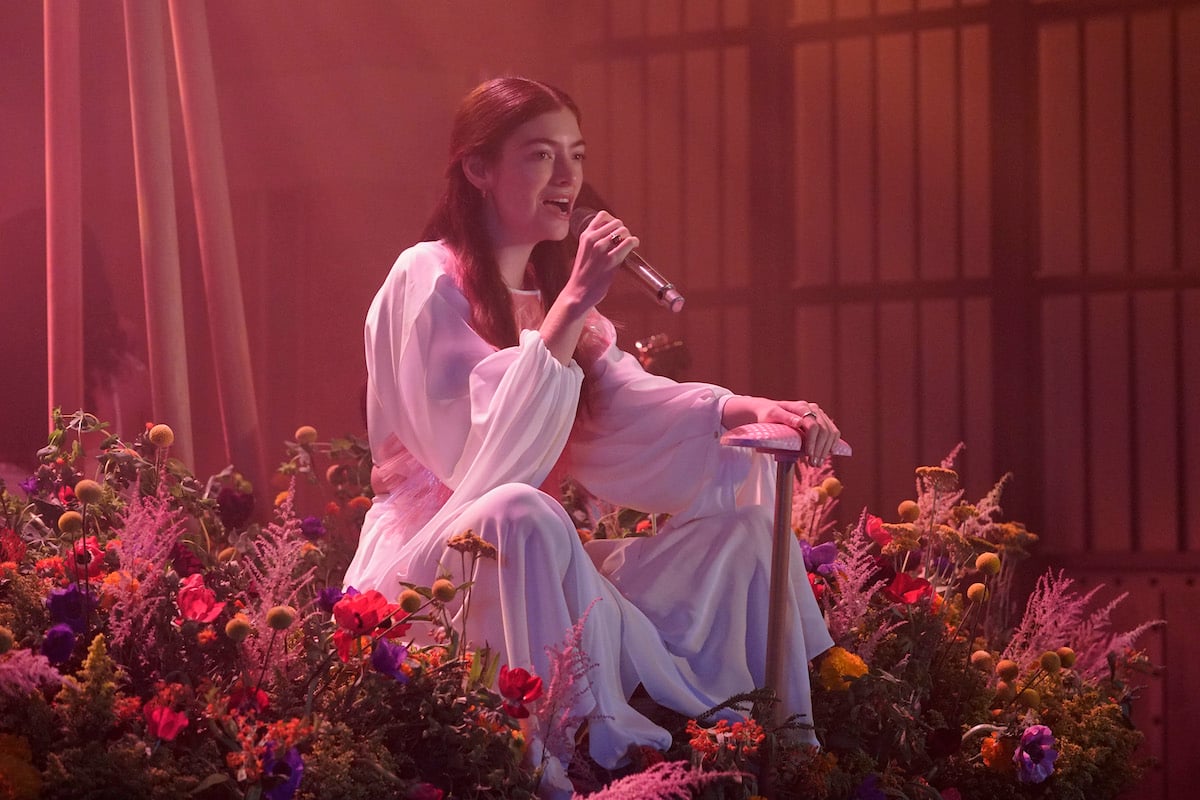 Lorde performing onstage in a field of flowers with red background lighting.
