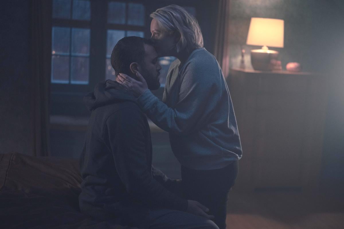 O-T Fagbenle and Elisabeth Moss as Luke and June in 'The Handmaid's Tale' Season 4 Episode 8. Fagbenle sits on a bed, Moss stands between his legs holding his head in her hands and kissing his forehead. They're in a bedroom at night.