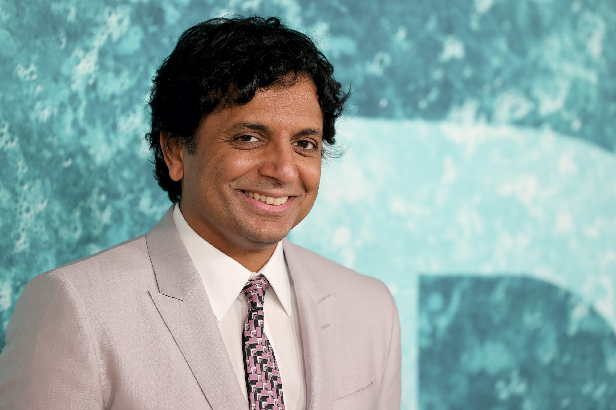 M. Night Shyamalan smiling in front of a blue background