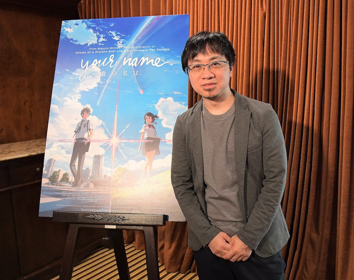 Makoto Shinkai poses next to a poster for his film ‘Your Name’