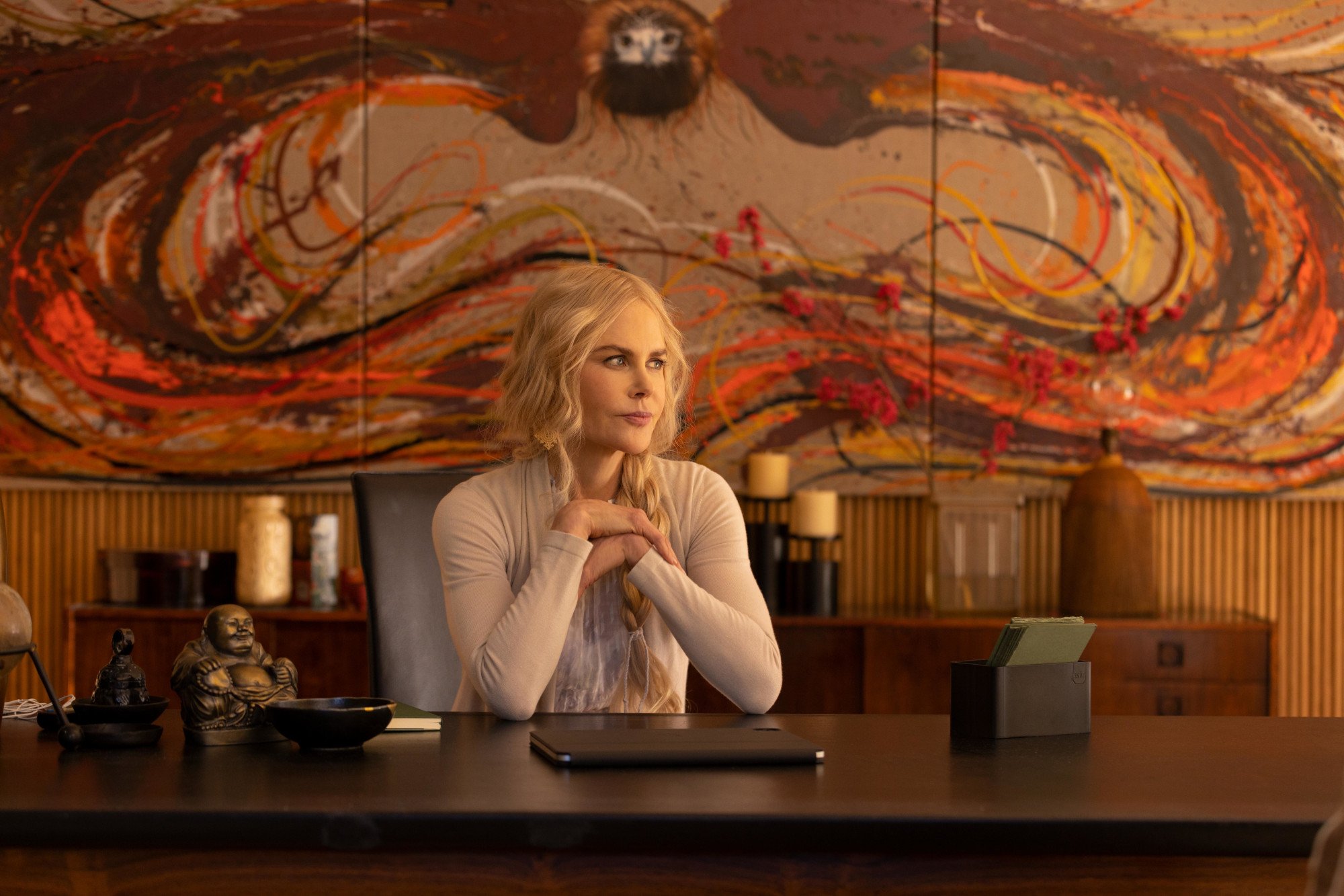 Nicole Kidman as Masha in Hulu's Nine Perfect Strangers. She's sitting at a desk with her hands clasped together, and she's looking sideways thinking. Fans have more than 1 theory about who's threatening her.