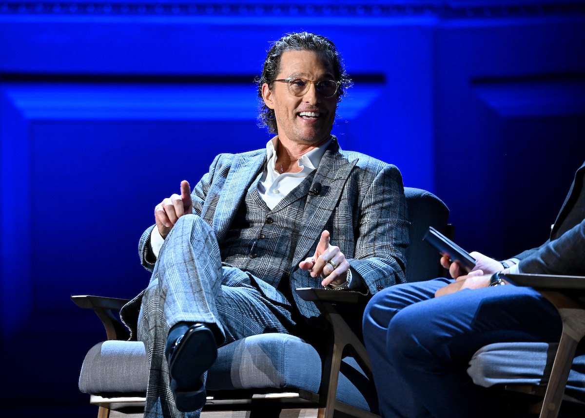 Matthew McConaughey in a plaid suit smiling and sitting in a chair on a stage