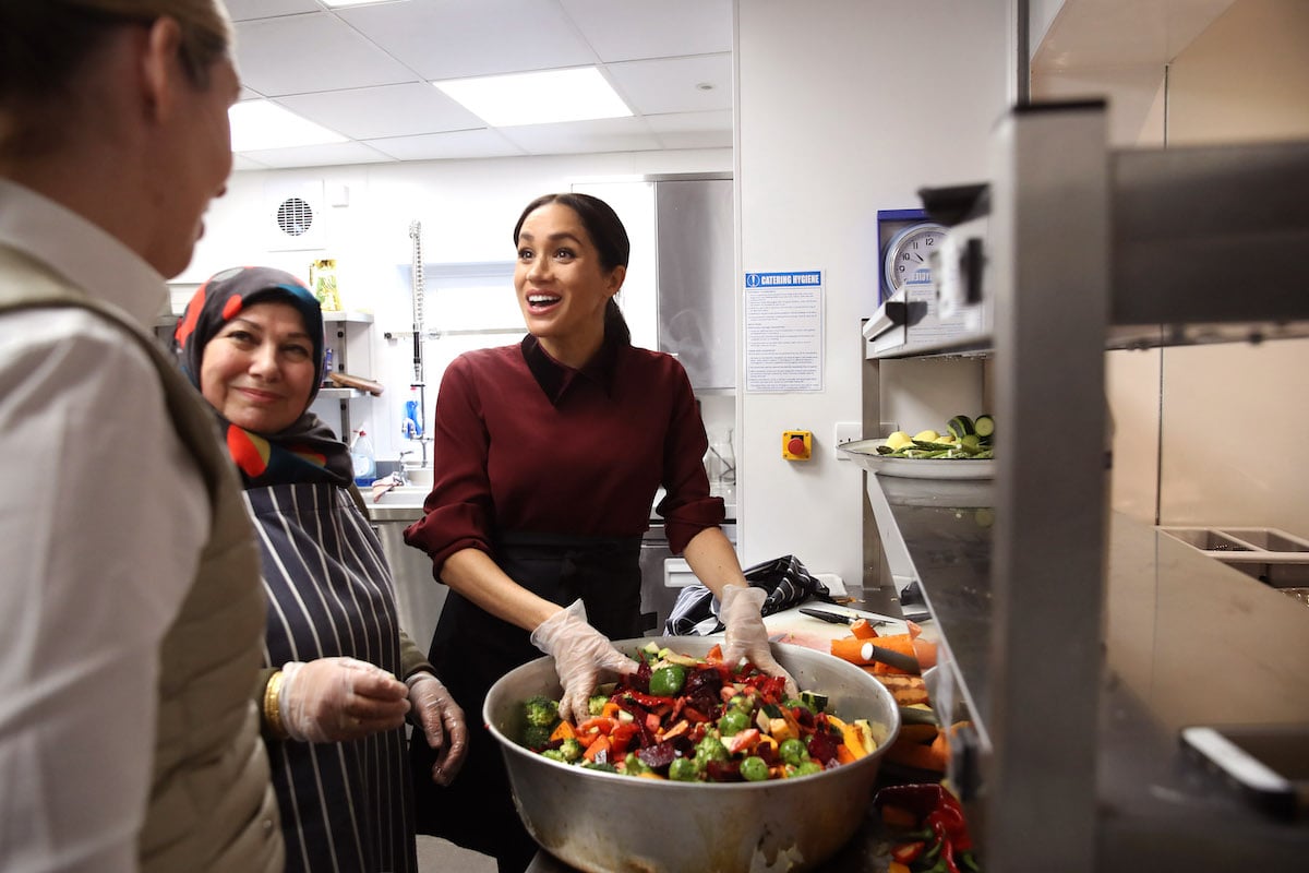 Meghan Markle smiles as she prepares food wearing rubber gloves at the Hubb Community Kitchen in 2018