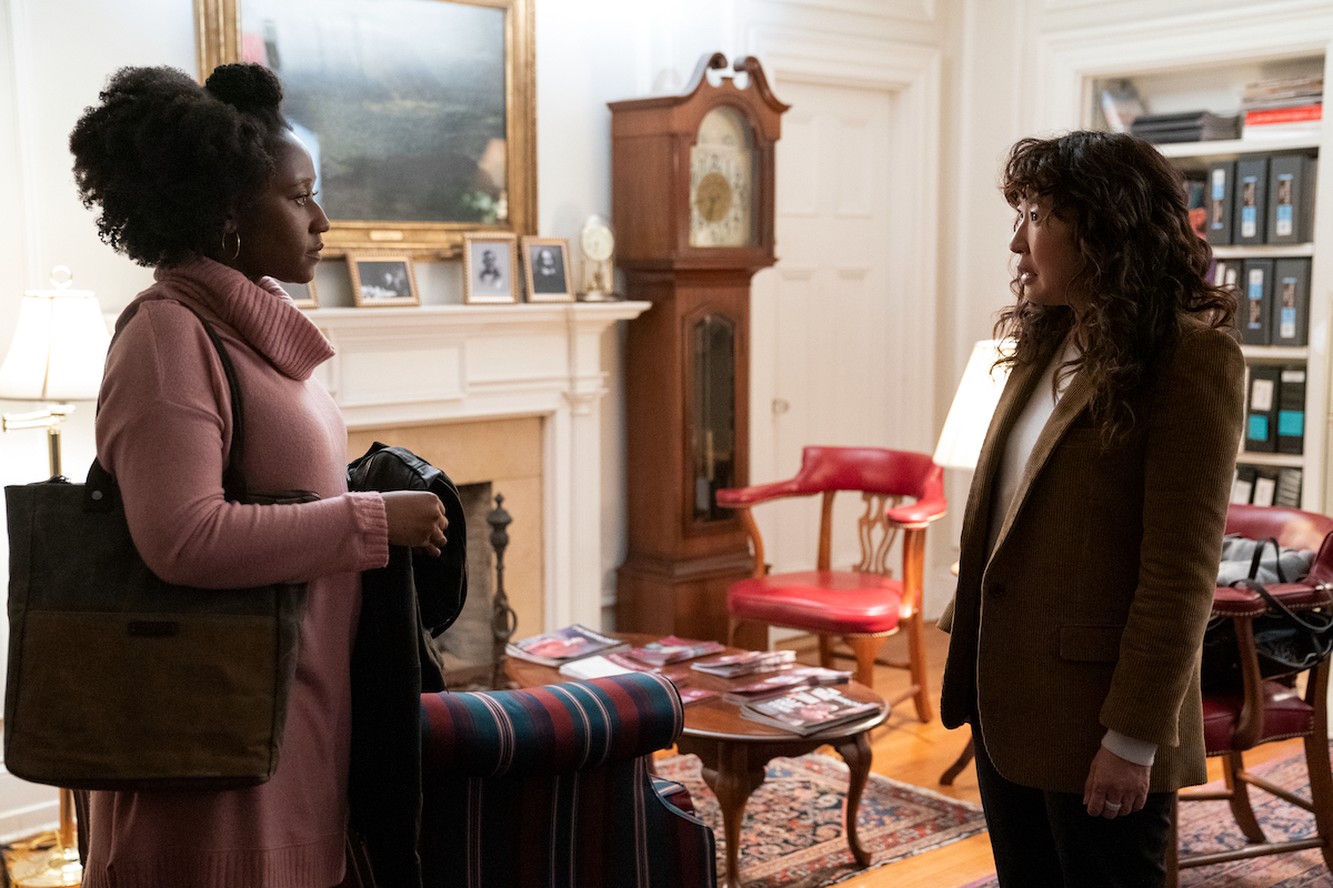 Nana Mensah wears a pink turtleneck sweater as she stands across from Sandra Oh in a brown suit in 'The Chair' Season 1