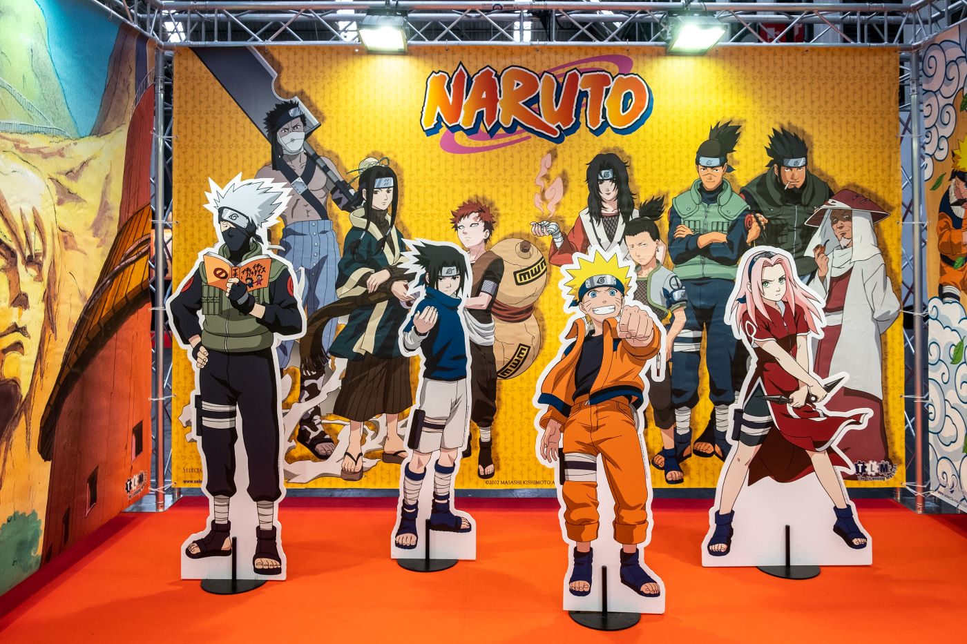 'Naruto' character cardboard cutouts in front of a background of more 'Naruto' characters.