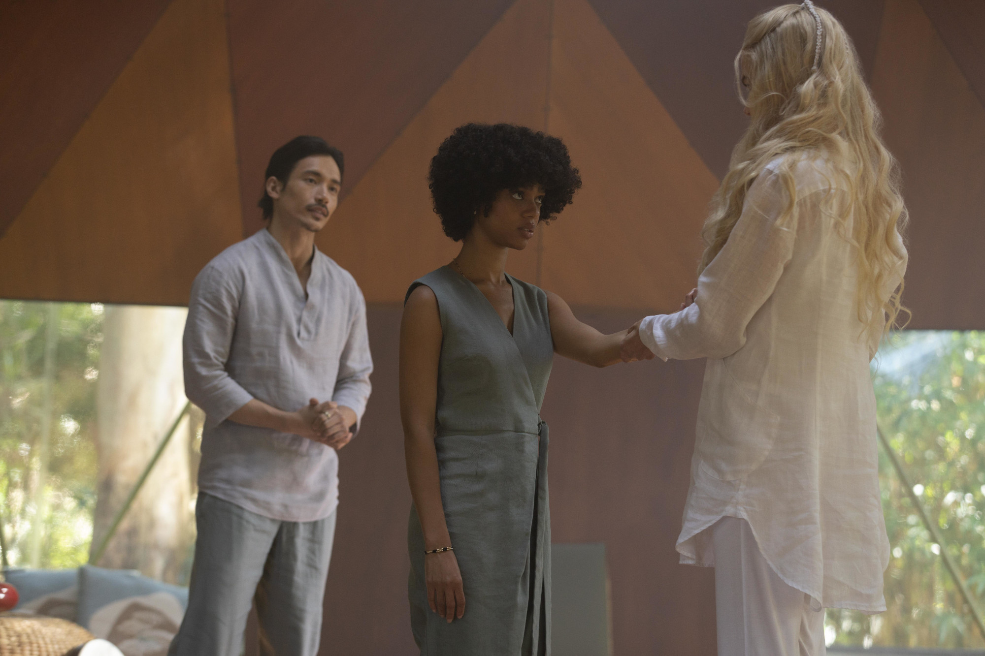 Manny Jacinto, Tiffany Boone, and Nicole Kidman in the cast of Hulu's 'Nine Perfect Strangers.' Jacinto's character wears all white and stands back while Boone's character, in grey, stares at Kidman. Kidman has her hand resting on Boone's shoulder, and she's turned away from the camera.