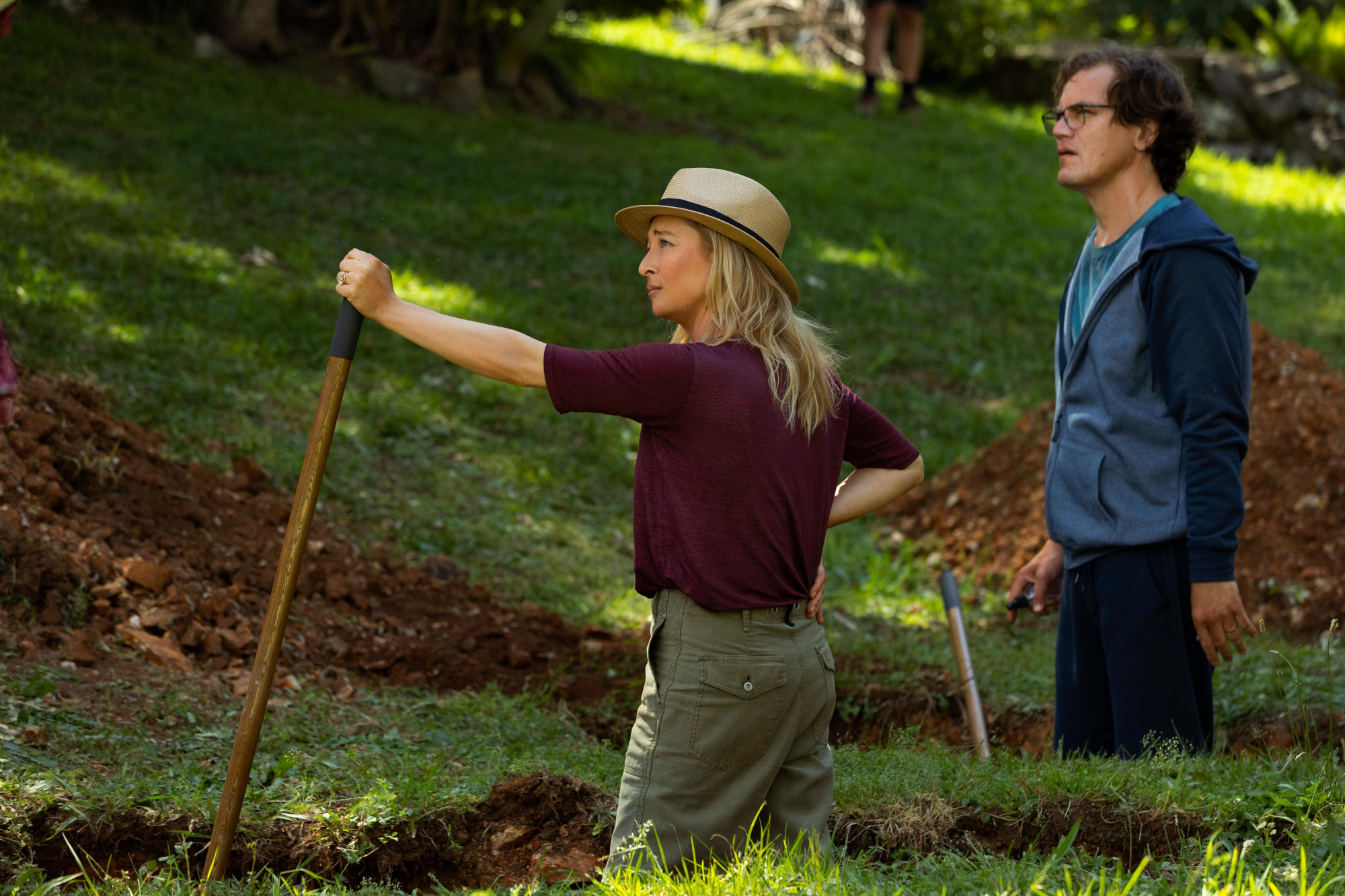Heather (Asher Keddie) and Napoleon (Michael Shannon) digging with shovels in Hulu's 'Nine Perfect Strangers.' The image shows their side profiles, and they're looking at something off-screen to the left.