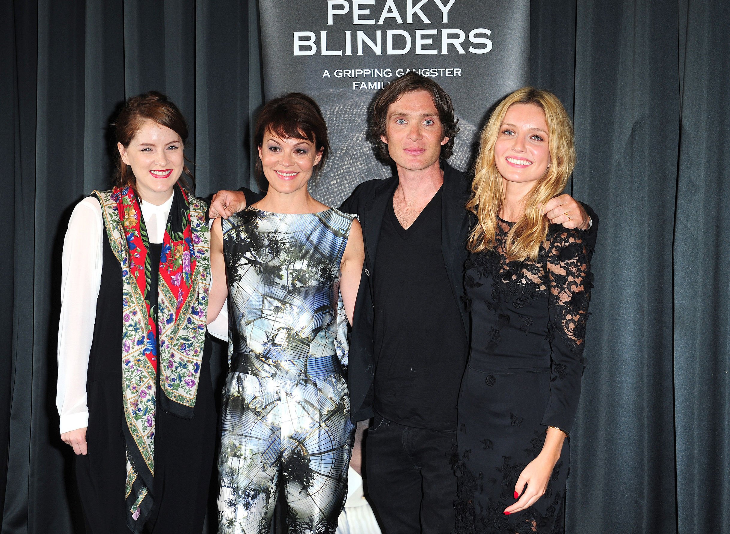 Sophie Rundle, Helen McCrory, Cillian Murphy, and Annabelle Wallis from 'Peaky Blinders' Season 6 standing next to each other in front of a show poster