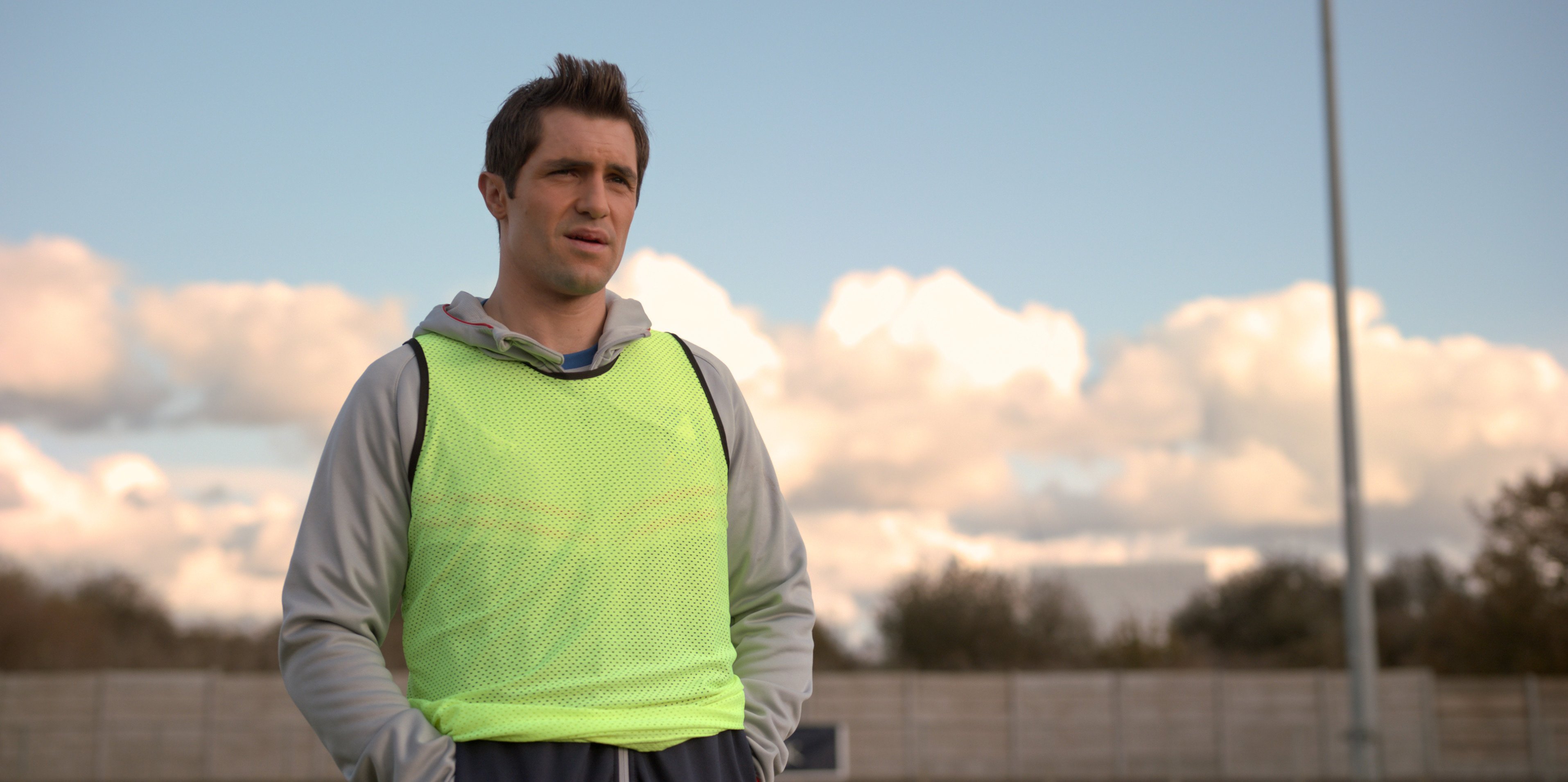 Phil Dunster wearing a yellow vest under a gray sweatshirt as Jamie Tartt on 'Ted Lasso'
