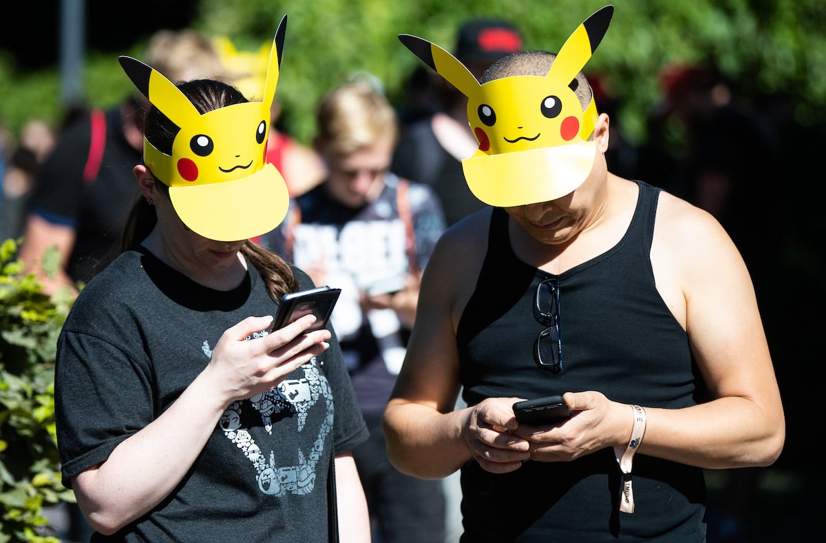 Two Pokemon Go players wearing Pikachu hats look down at their phones and play the game.