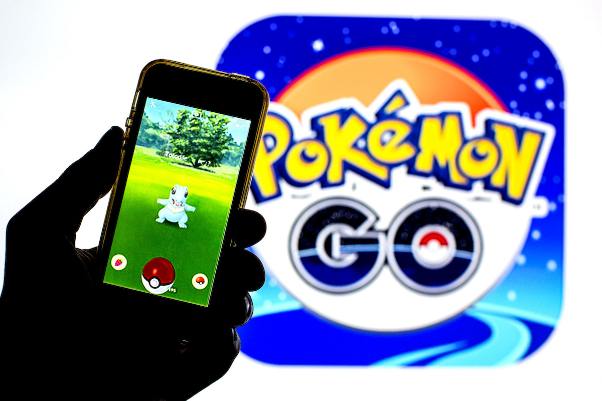 A dark cartoon hand holds a phone displaying the Pokemon go game on the screen.