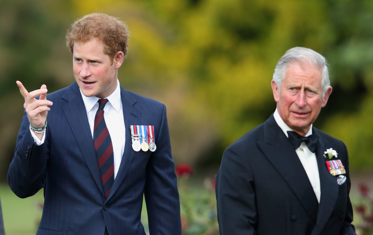 Prince Harry pointing to something off-camera, while walking alongside Prince Charles