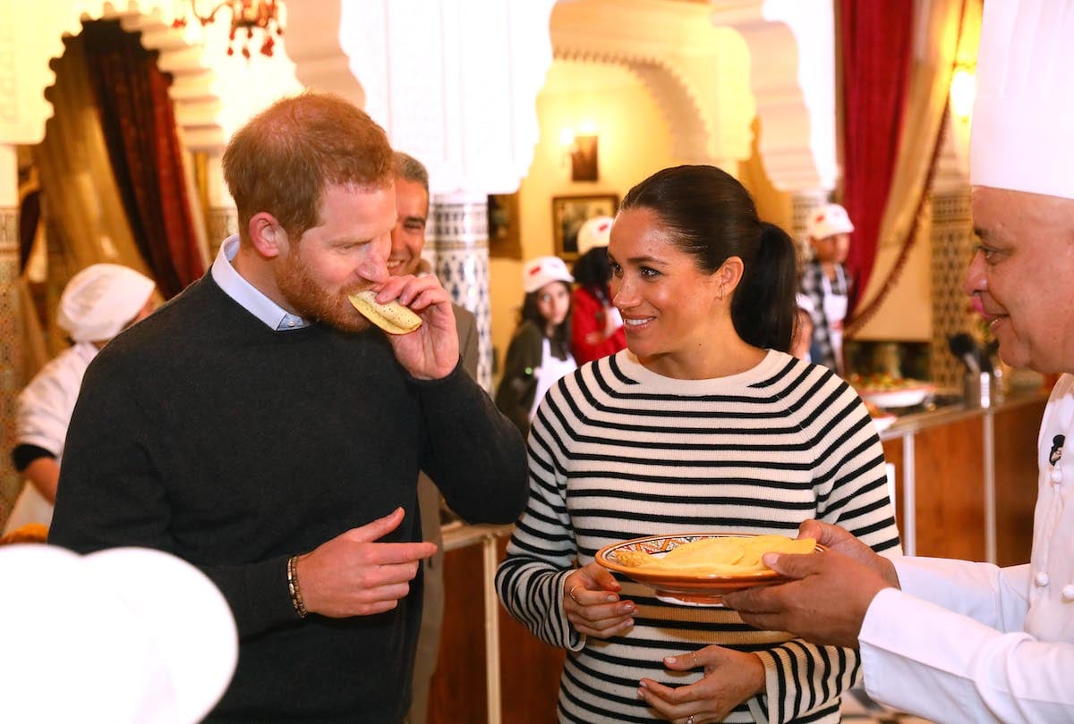 Meghan Markle smiles as Prince Harry takes a bite of food at a cooking demonstration in Morocco in 2019