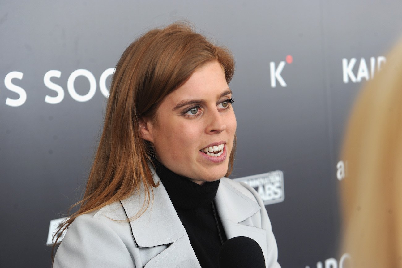 Princess Beatrice speaking into microphone in front of gray background