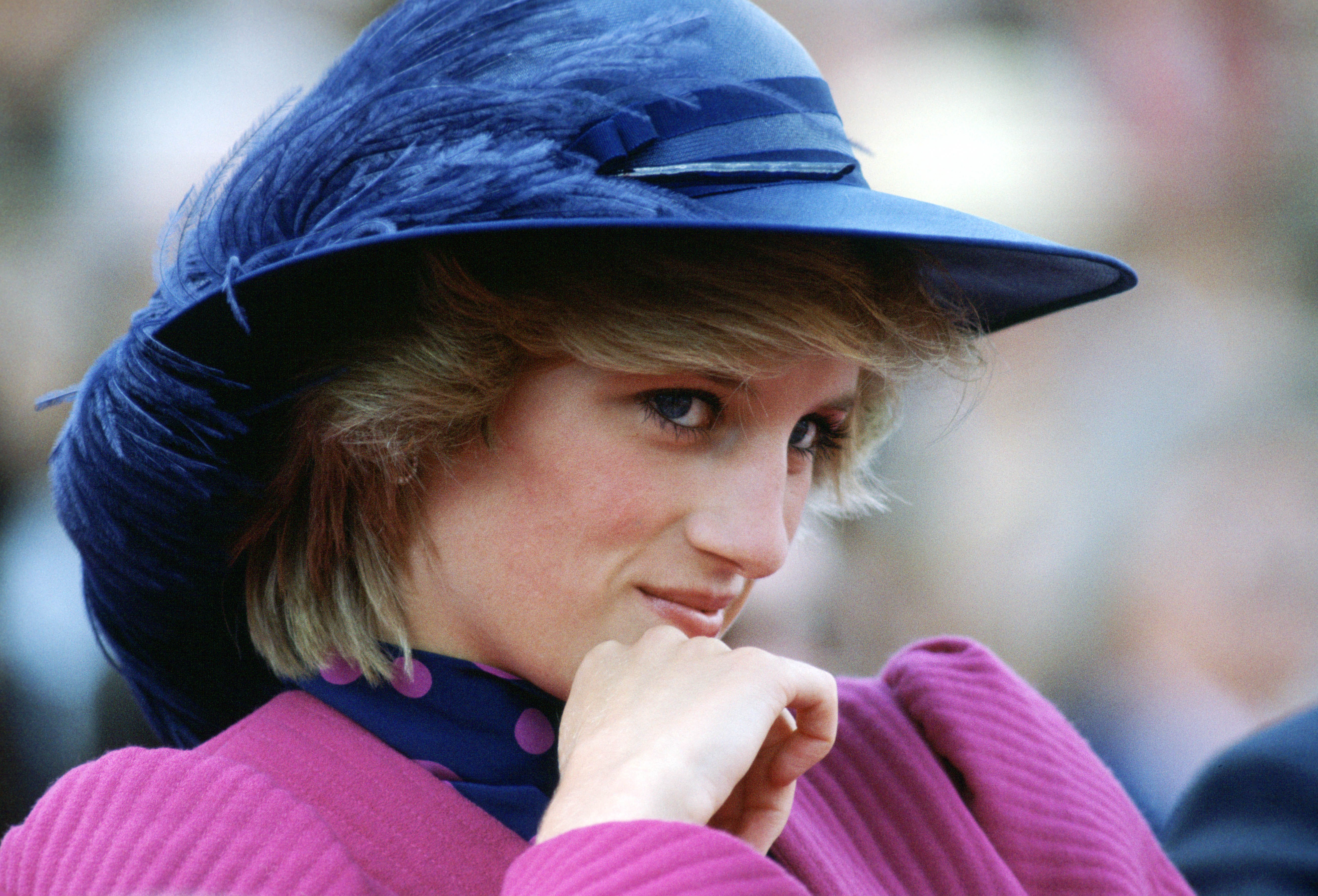 Princess Diana wearing a feathered blue hat and holding her hand up to her chin