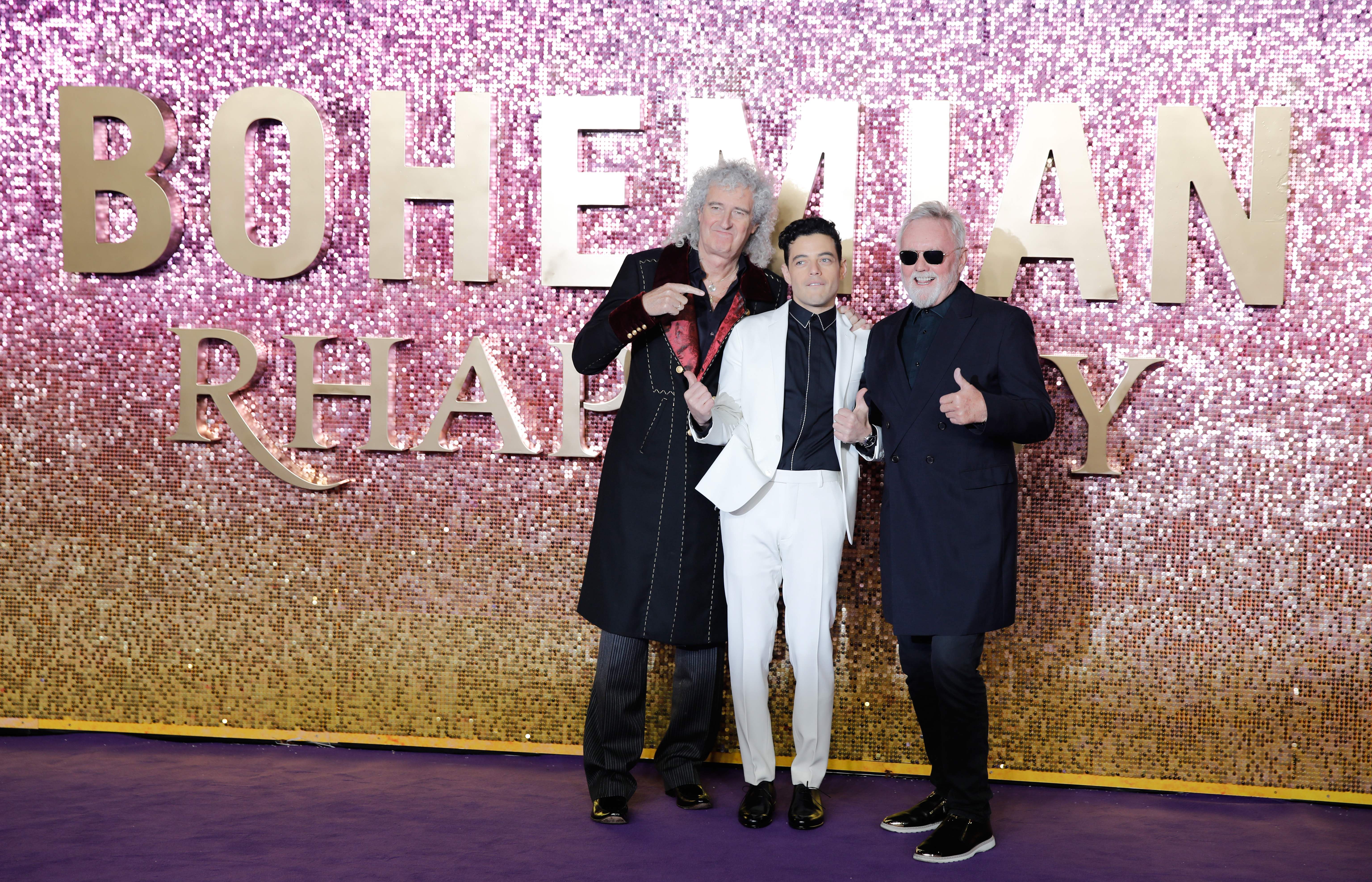 Rami Malek, Roger Taylor and Brian May smiling on the red carpet