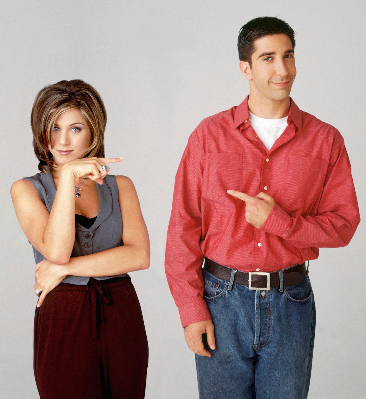 Jennifer Aniston and David Schwimmer stand facing the camera and smiling while pointing at each other.