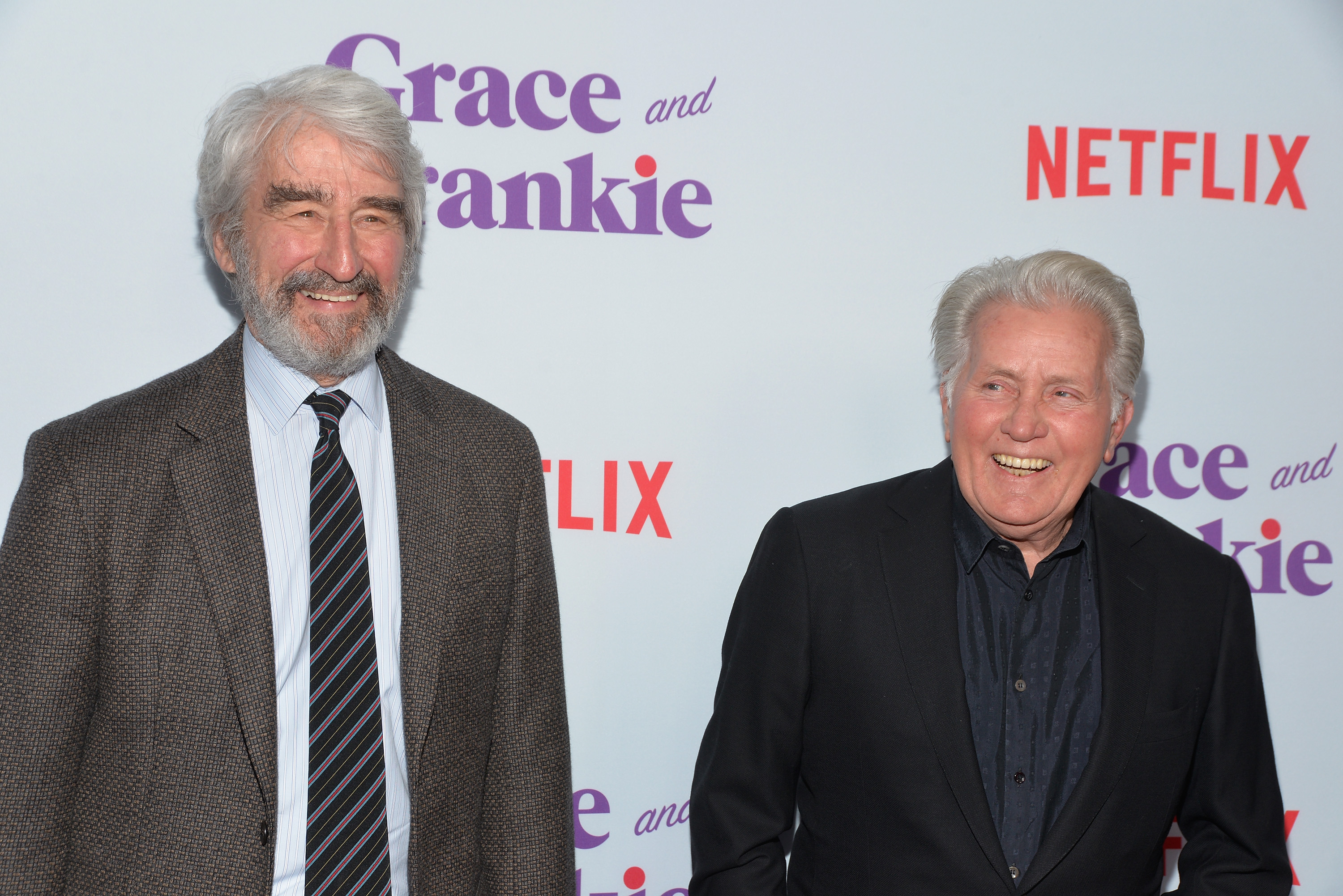 Sam Waterston and Martin Sheen laugh while taking a photo together.