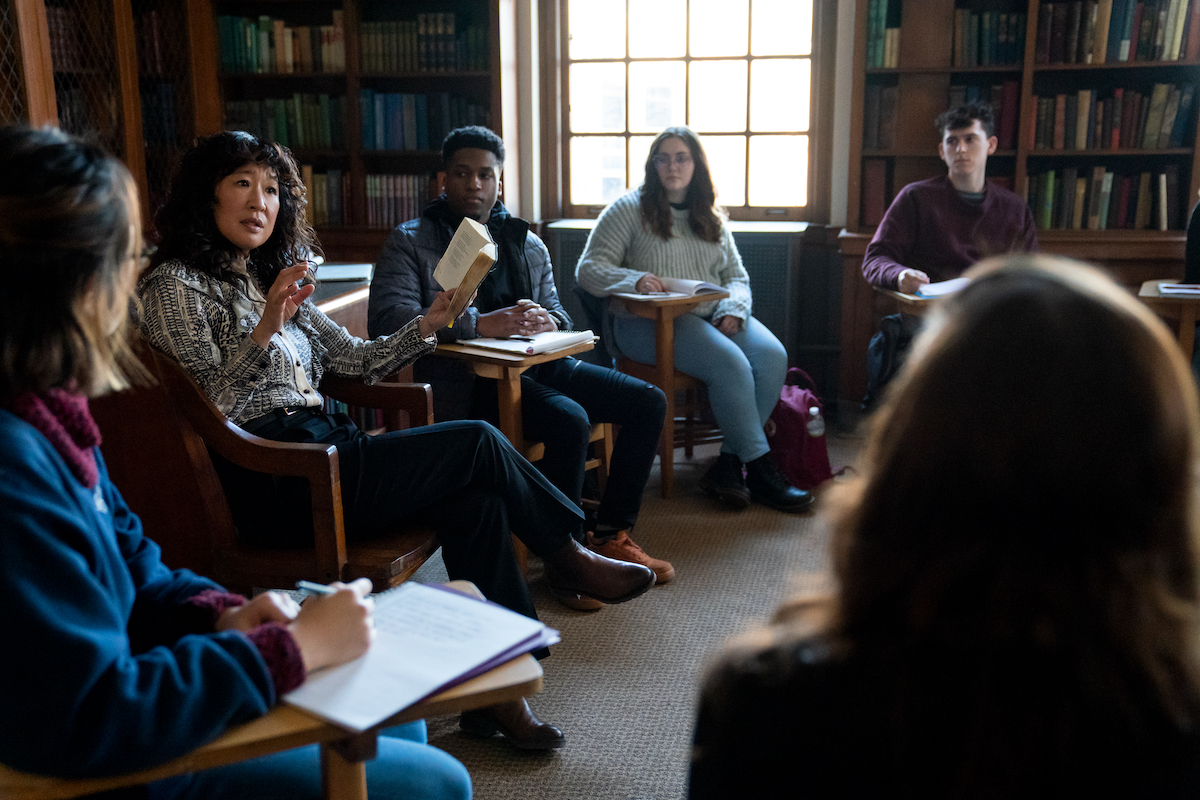 Sandra Oh sits in a chair reading from a book as students sit in desks around her in 'The Chair' Season 1 Episode 6