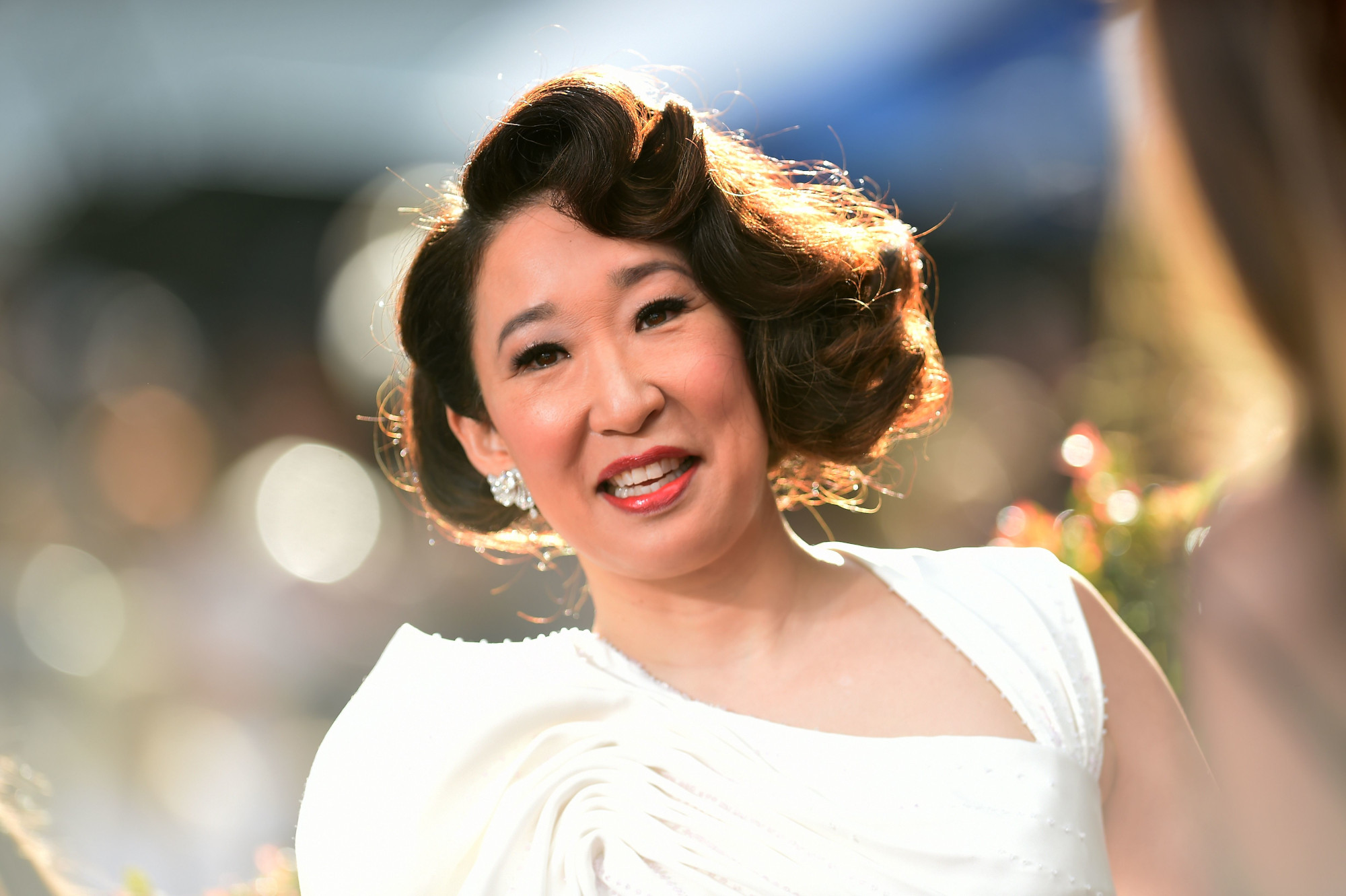 'Grey's Anatomy' star Sandra Oh wearing a white dress. Her hair is curled and she's smiling. The background behind her is blurred.