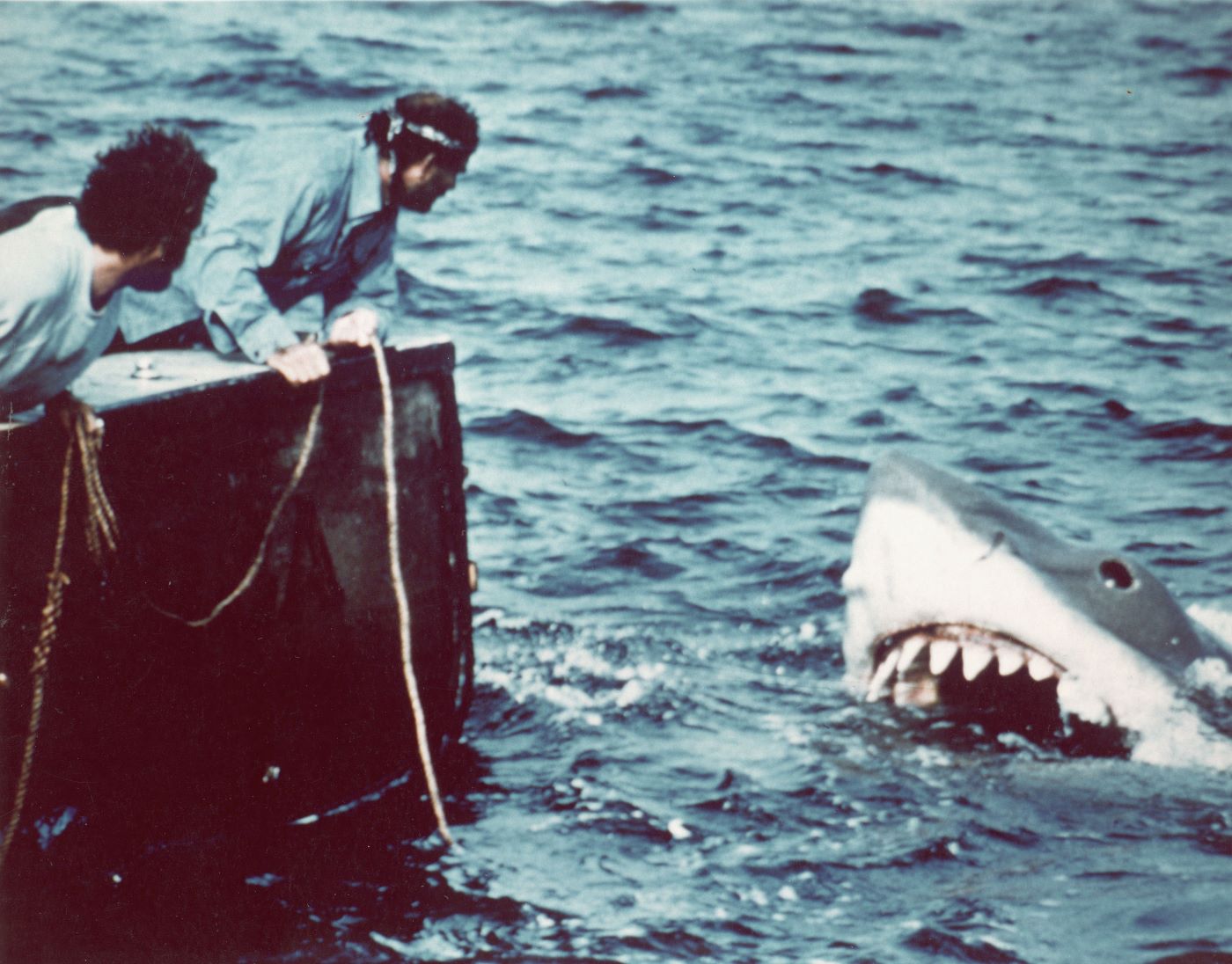 Scene from Steven Spielberg's 'Jaws' with the shark coming out of the ocean and two men leaving over the bow of the boat to look.