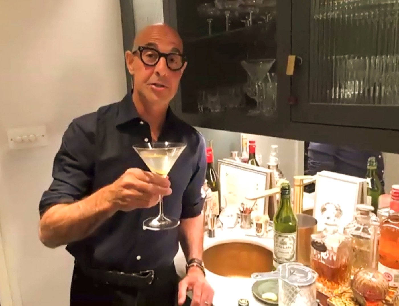 Stanley Tucci holds up a cocktail he made in his kitchen over a Zoom call.
