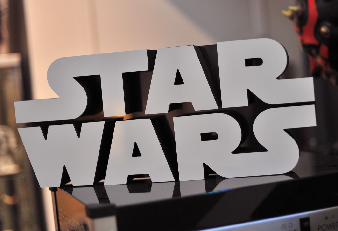 Star Wars text in grey sitting on a shiny black surface with a white background.