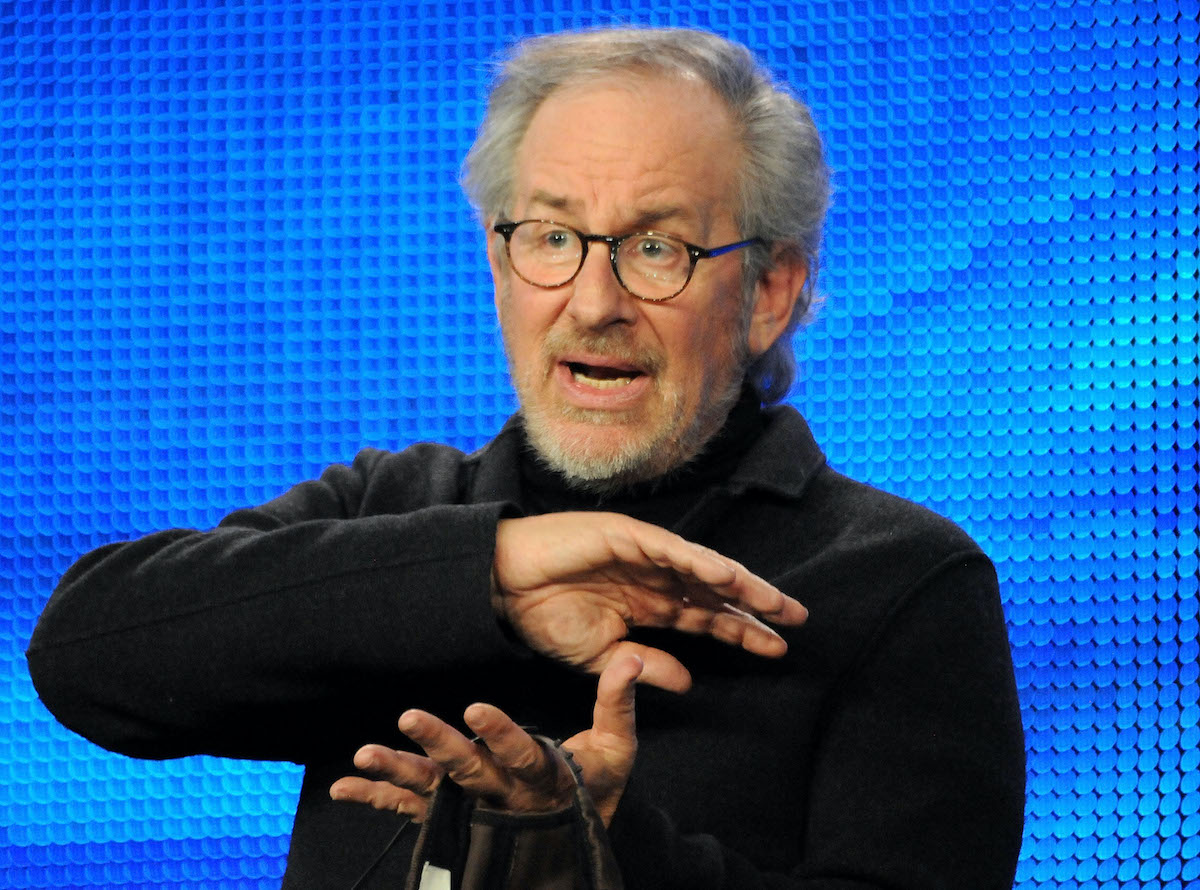 Steven Spielberg holds his hands up while he talks in front of a blue background