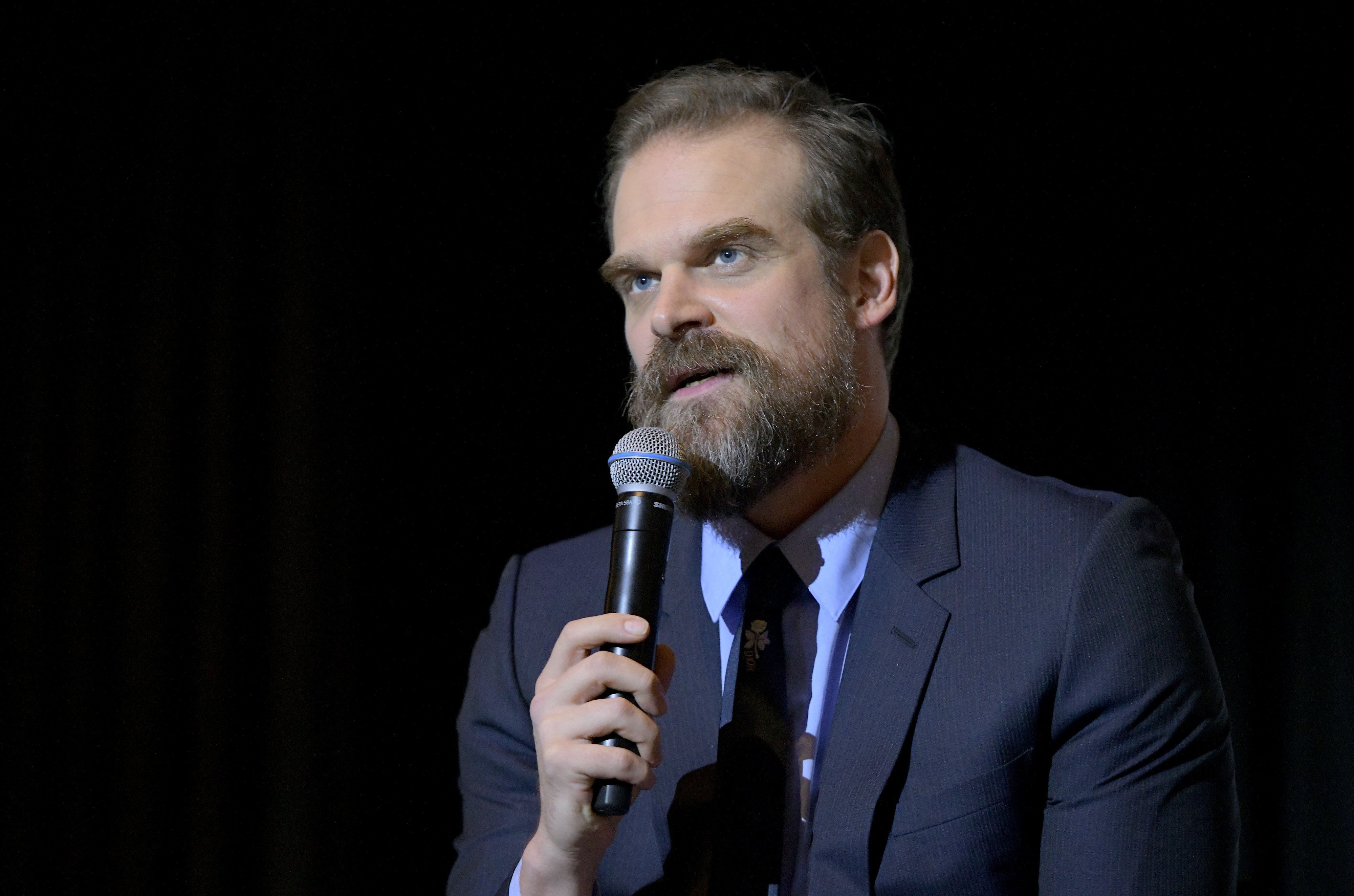 David Habour in a navy suit holding a microphone.