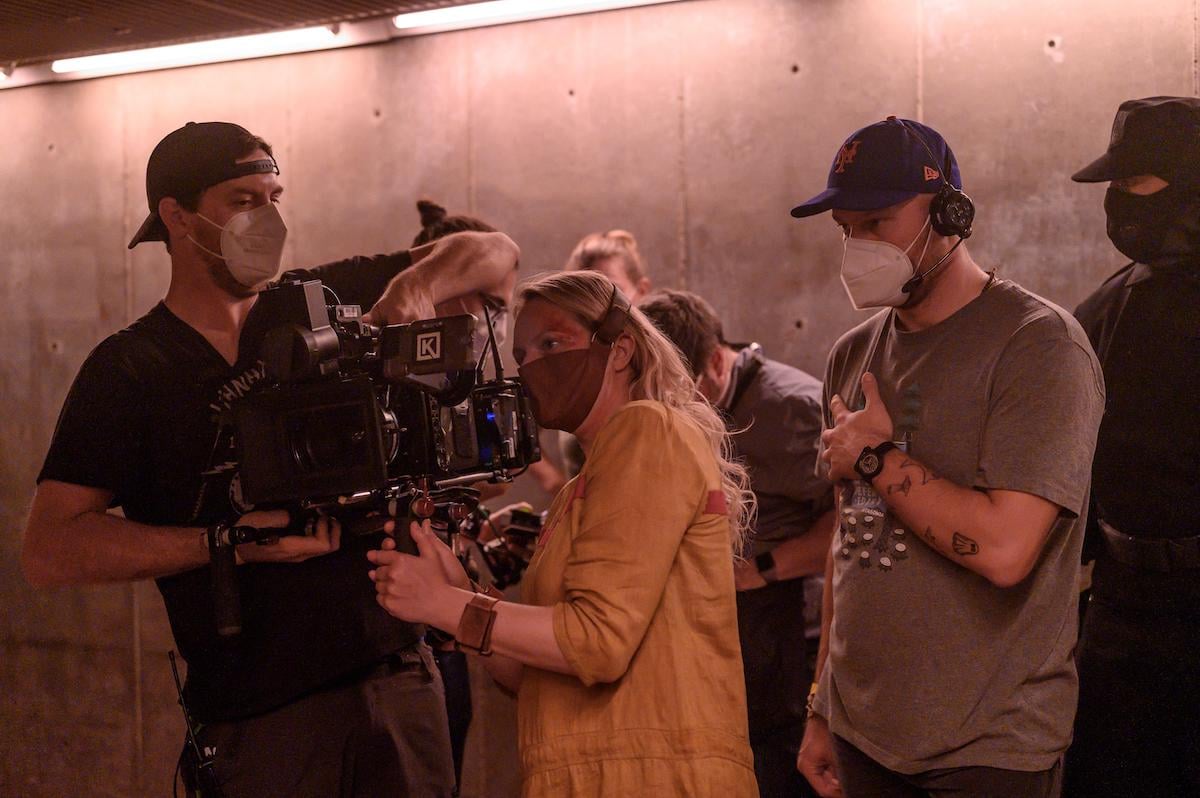 Elisabeth Moss and crew behind-the-scenes of 'The Handmaid's Tale' Season 4 Episode 3, 'The Crossing.' Moss directed this episode. And in the photo, she's dressed as June, who's being tortured in a high-security Gilead prison and wearing a mask and yellow prison dress. Moss is looking at playback on a video camera and is surrounded by other crew members dressed in casual clothing and masks.