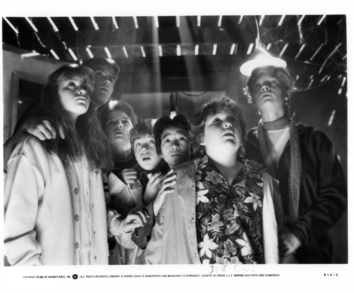 Several characters from 'The Goonies' gathered together underneath a floor looking up in this black and white picture.