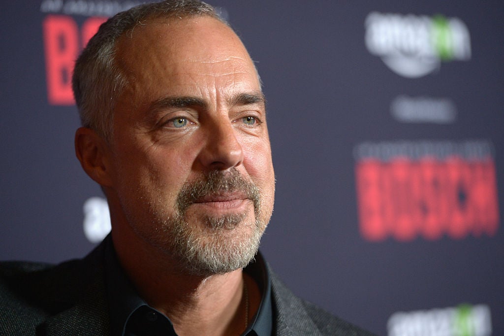 Titus Welliver walks the red carpet in a dark suit. 'Bosch' is written on the wall behind him.