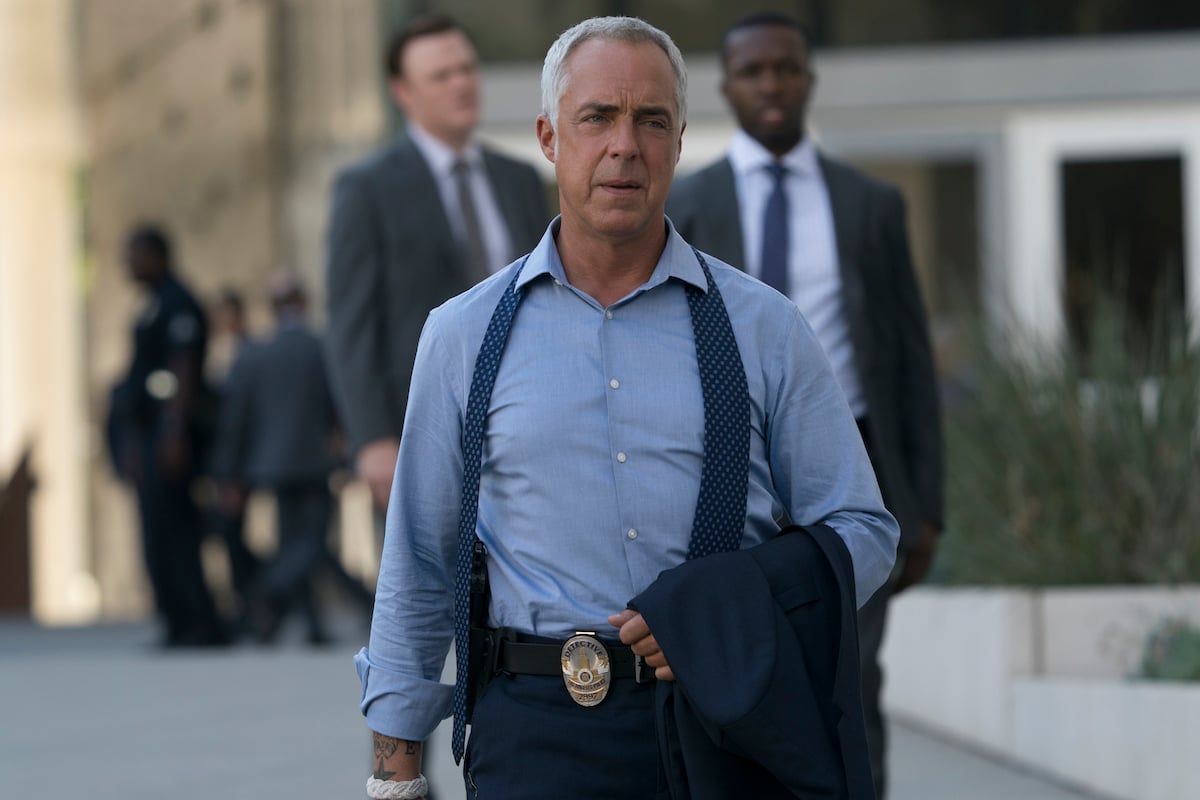 Titus Welliver as Harry Bosch walks the street holding his jacket in hand.