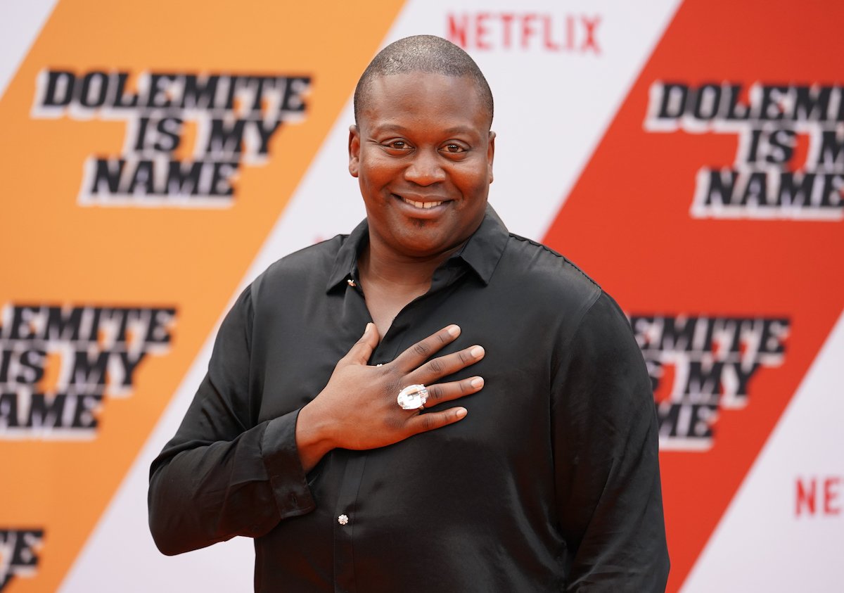 Tituss Burgess smiles for the camera with his hand on his heart.