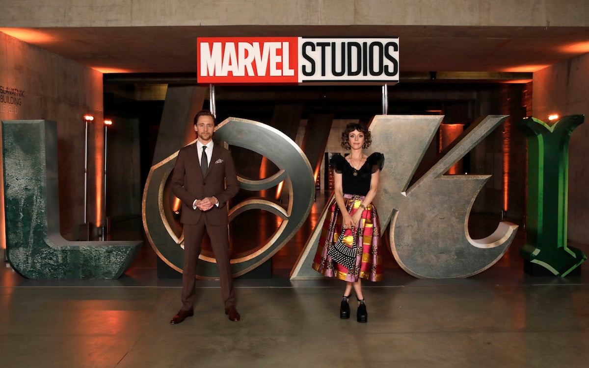 Tom Hiddleston and Sophia Di Martino in front of Loki logo.