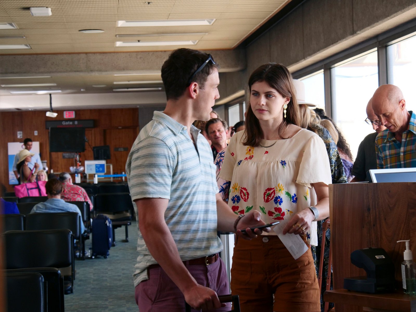 Jake Lacy and Alexandra Daddario in 'The White Lotus' finale. Lacy's character wears a blue and white striped polo and is looking at Daddario. She's wearing a beige shirt with flowers and has red eyes from crying. They're standing in an airport.