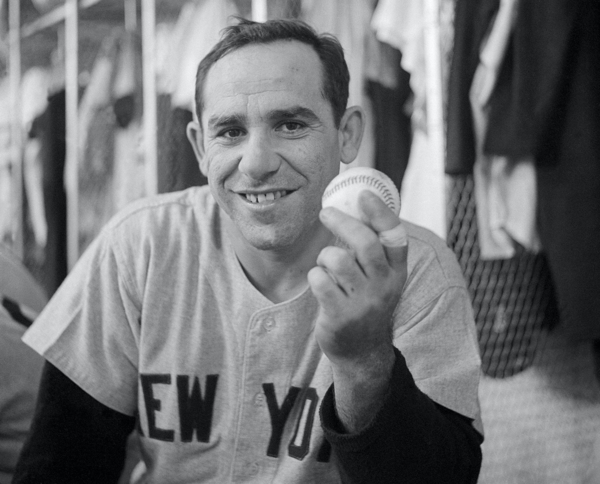 Yogi Berra smiling in his Yankee uniform, holding a baseball, in black and white