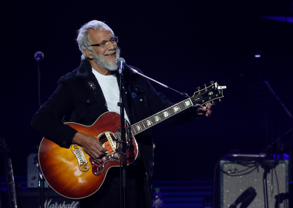 Yusuf Islam performs onstage, singing and playing the guitar.