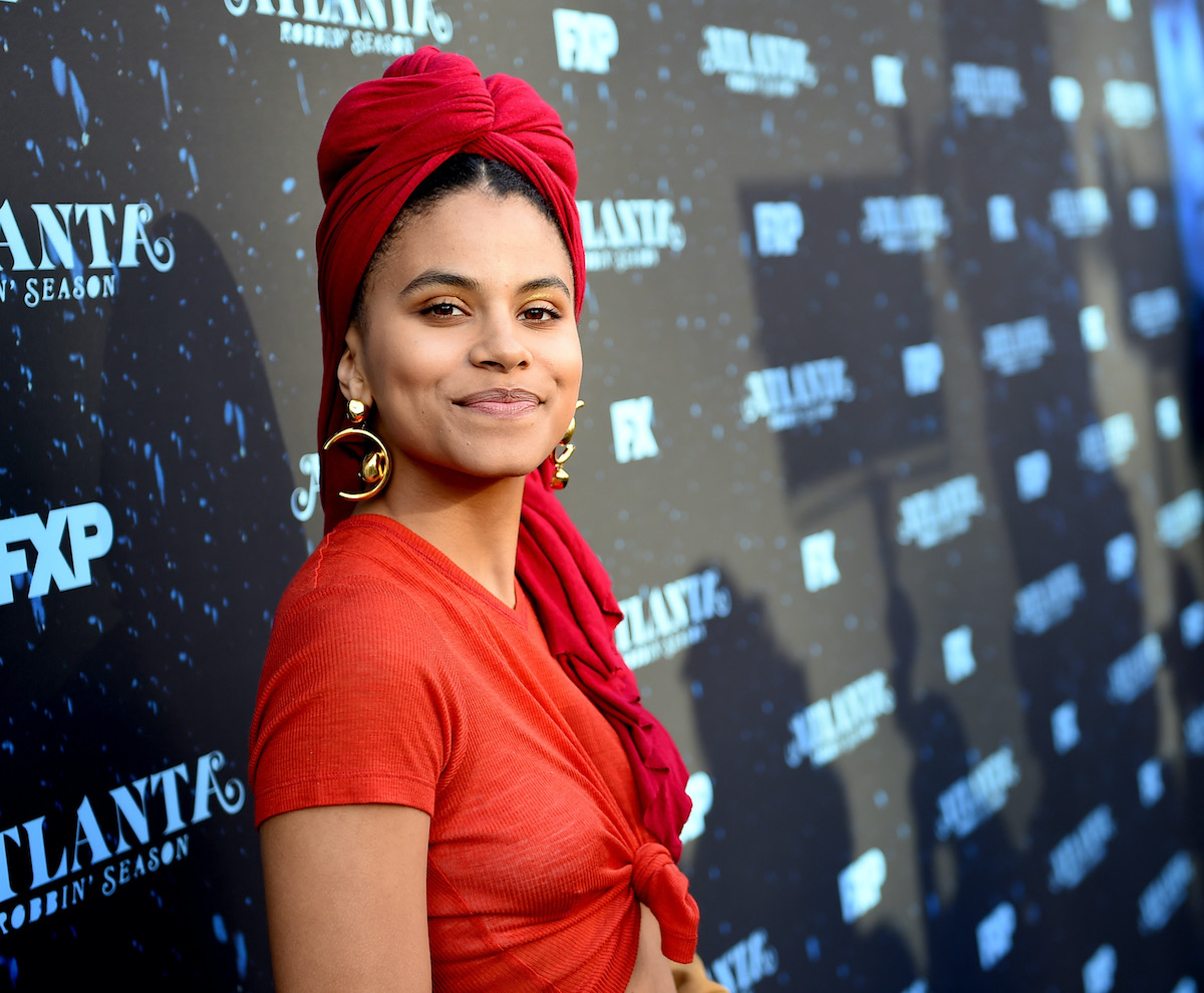 Zazie Beetz poses on the red carpet at an event for 'Atlanta' in a red dress and matching headpiece