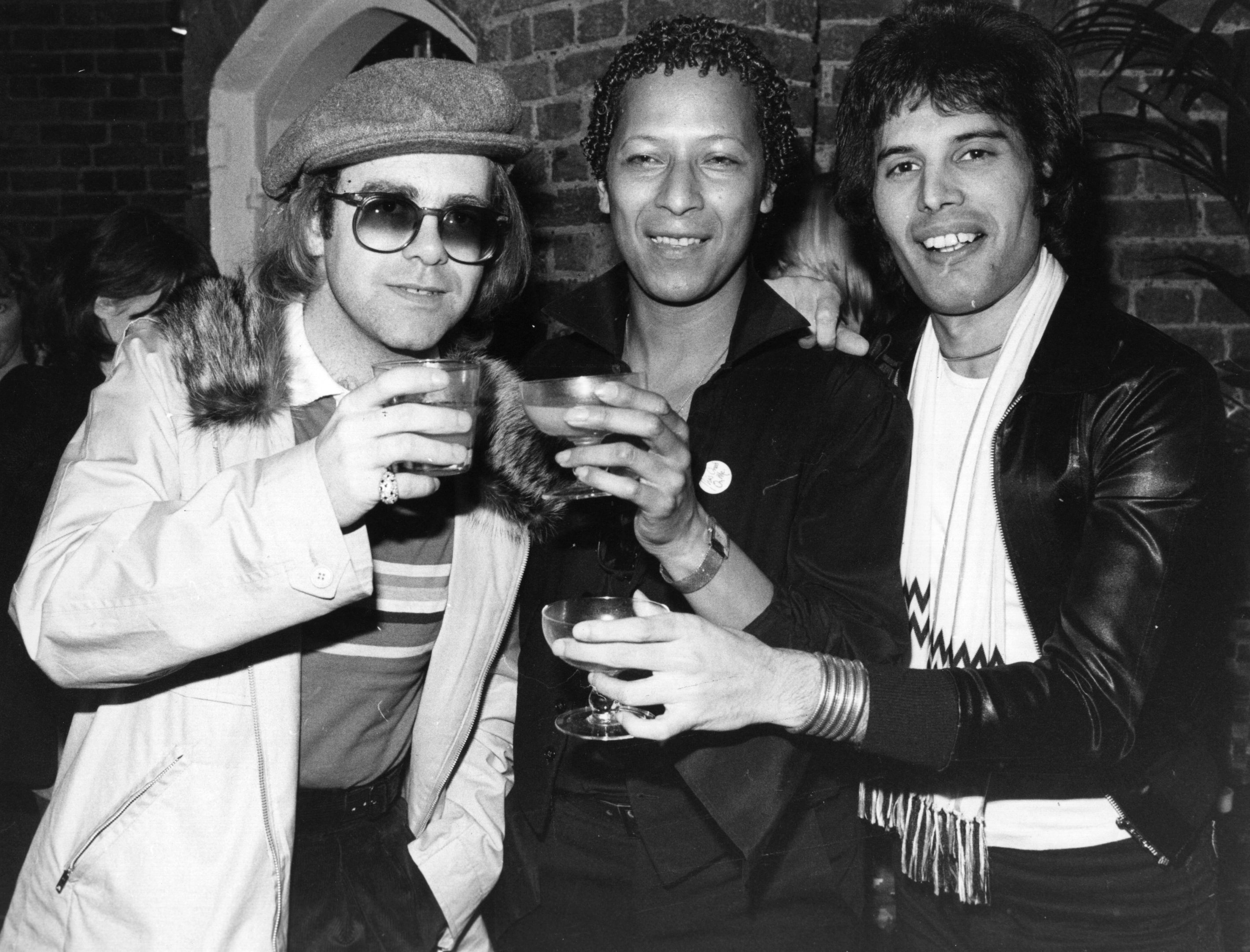 Elton John, Peter Straker, and Freddie Mercury holding glasses