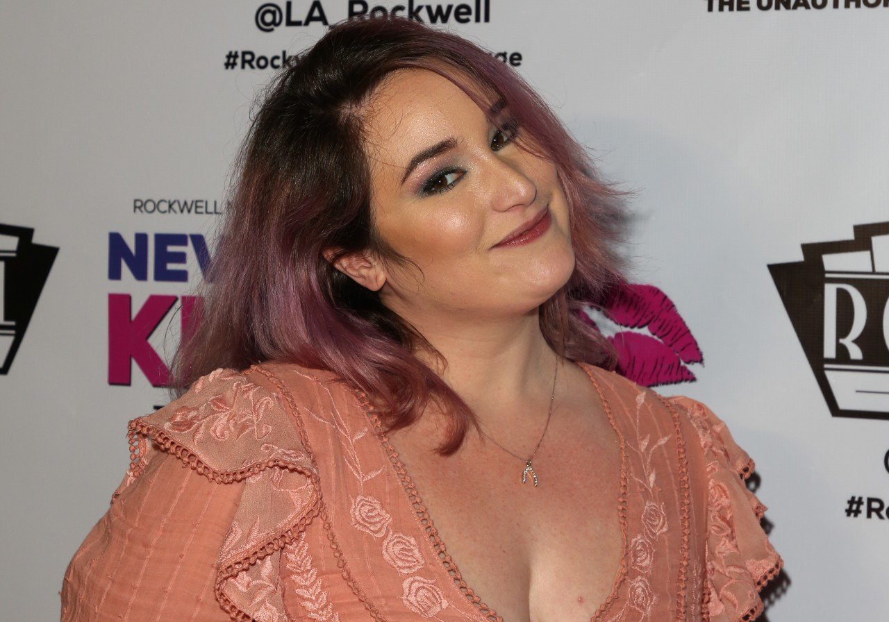 Emma Hunton smiles while wearing a peach outfit at a media event.