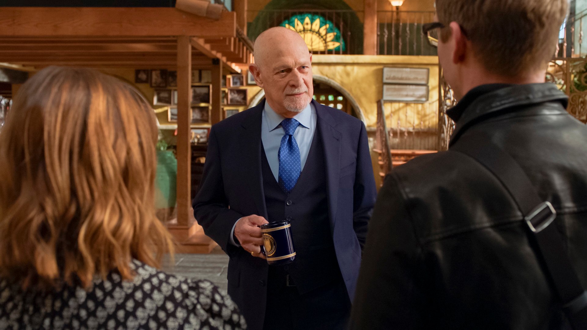 Gerald McRaney as Admiral Hollace Kilbride holding a mug and talking to Renee Felice Smith and Barrett Foa on the set of NCIS LA.