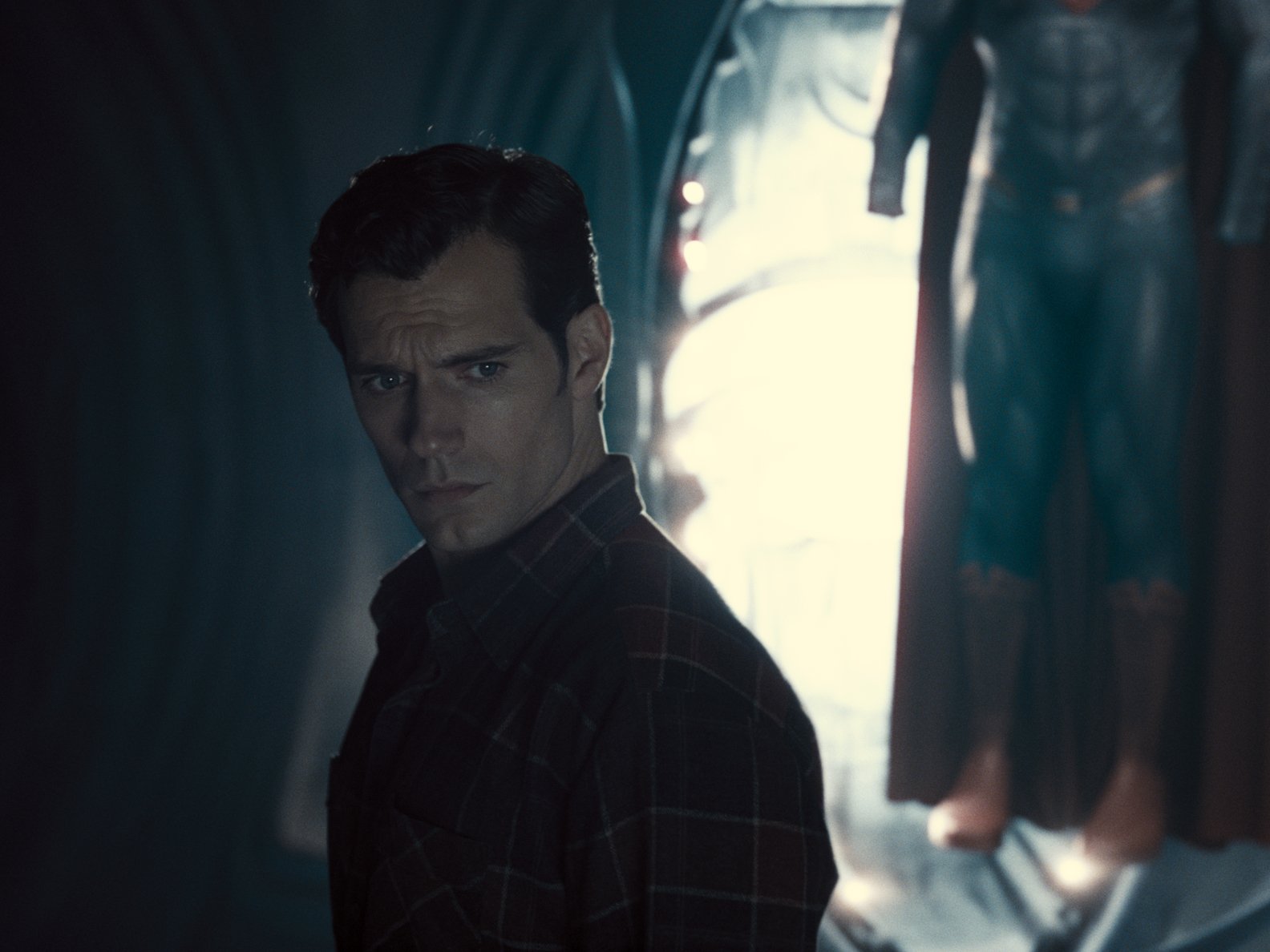 Henry Cavill as Superman/Clark Kent in 'Zack Snyder's Justice League.' He's wearing a black flannel shirt and the Superman suit is in the background