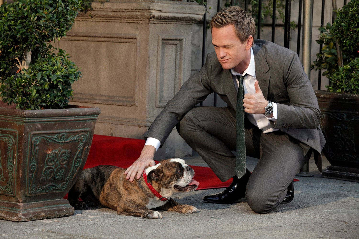 Neil Patrick Harris as Barney Stinson petting a dog and winking at the camera in 'How I Met Your Mother'