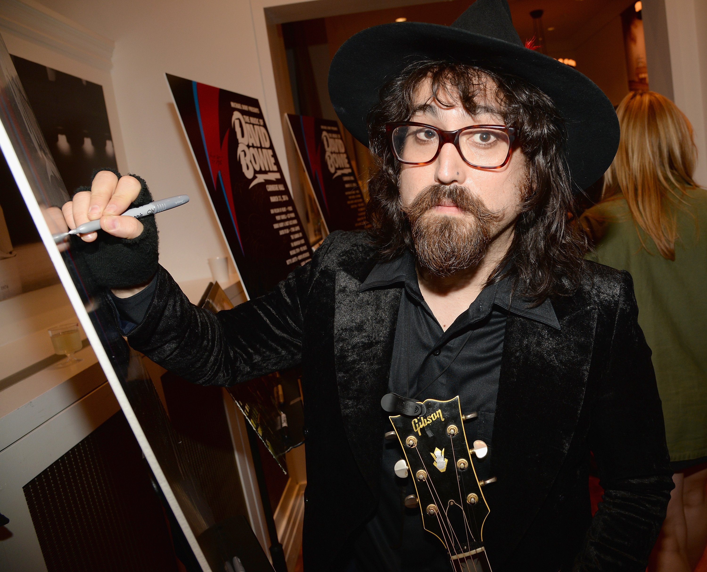 Sean Lennon signing a poster with a marker